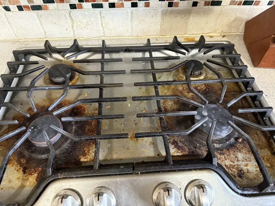 A gas stovetop with grease and burnt food before cleaning
